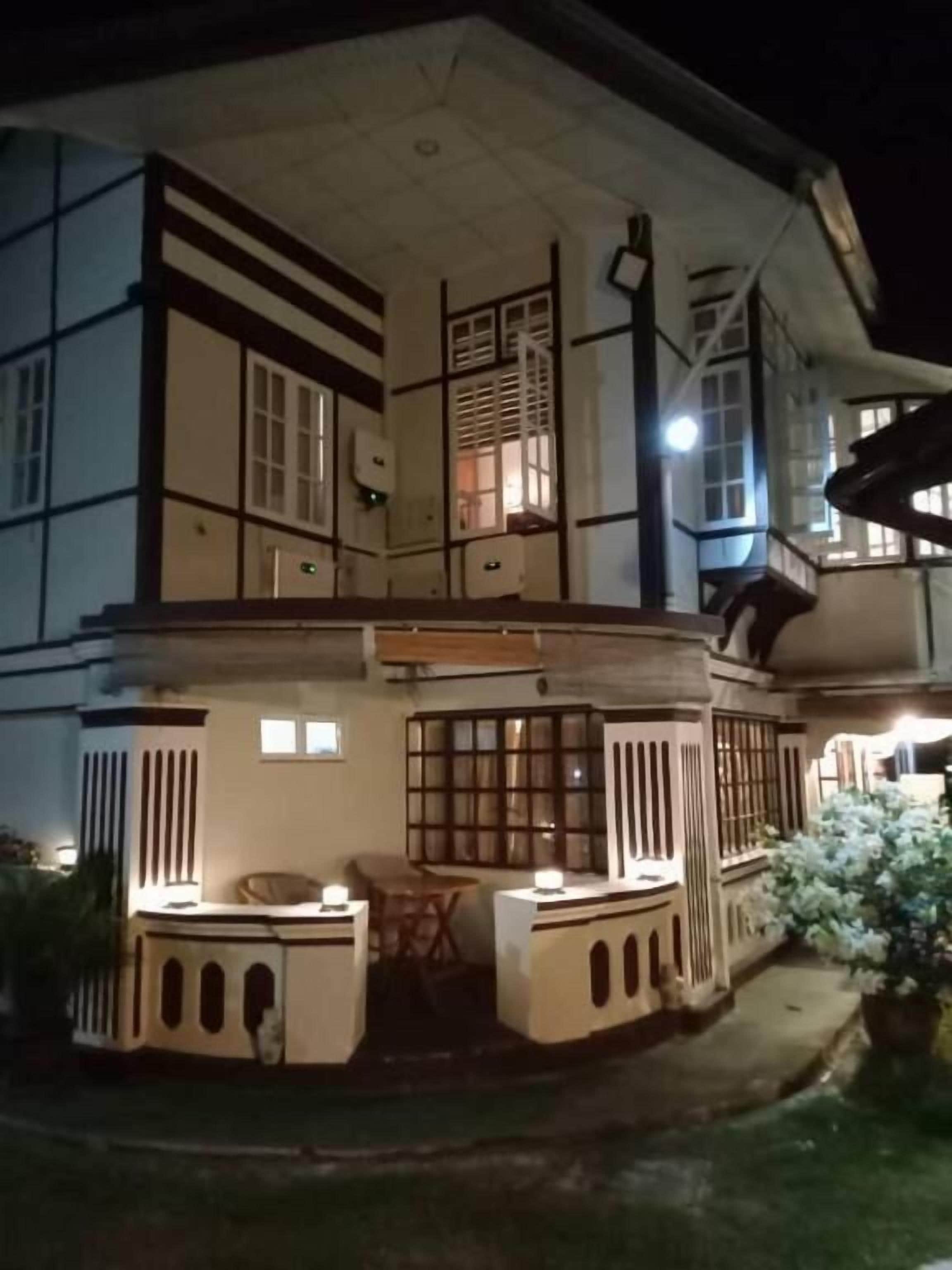 Um edifício de dois andares com varanda, janelas amplas e área externa bem iluminada para sentar.