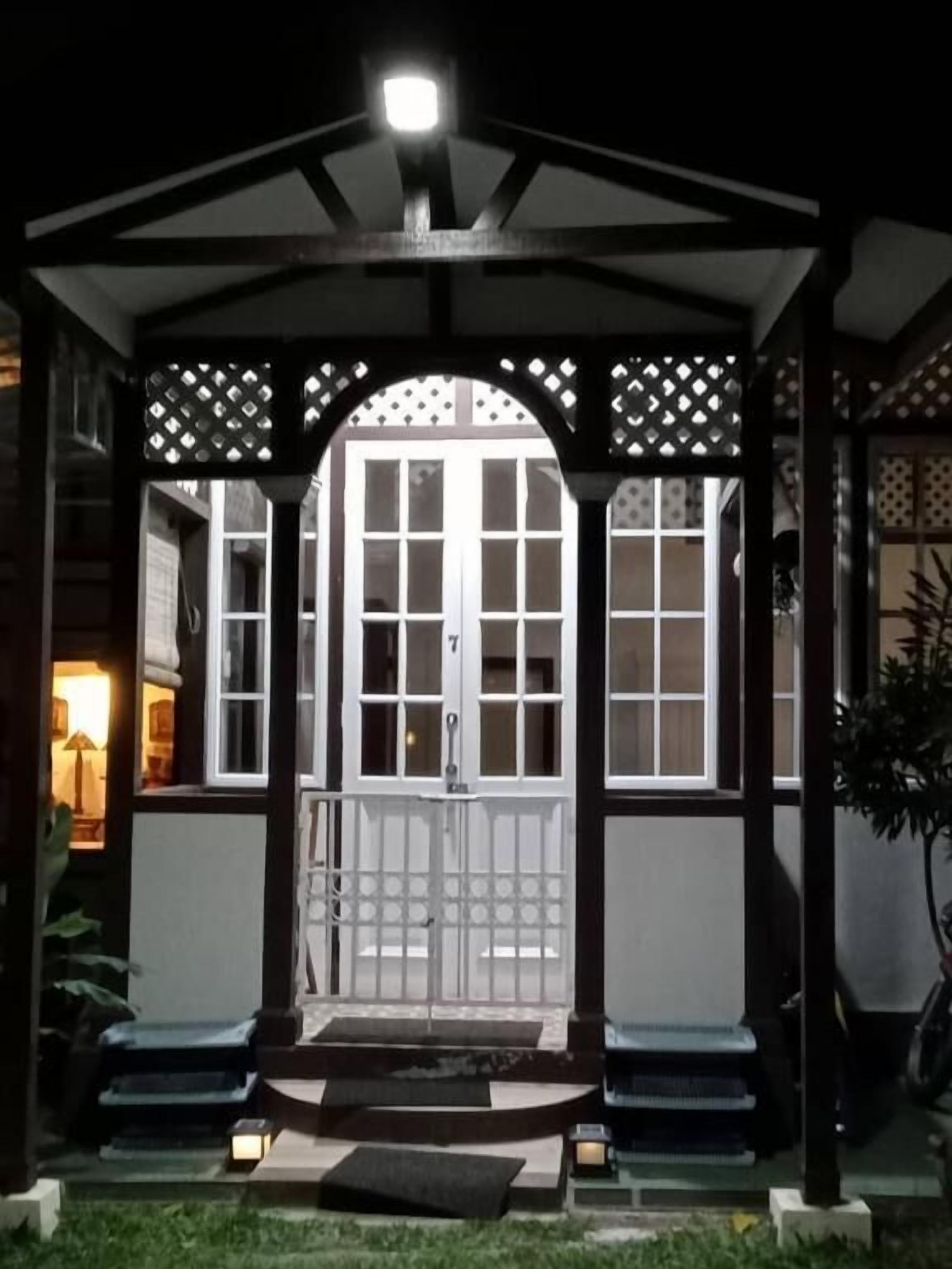 A covered entrance with a wooden archway, a white door with a number, and steps leading up to it.