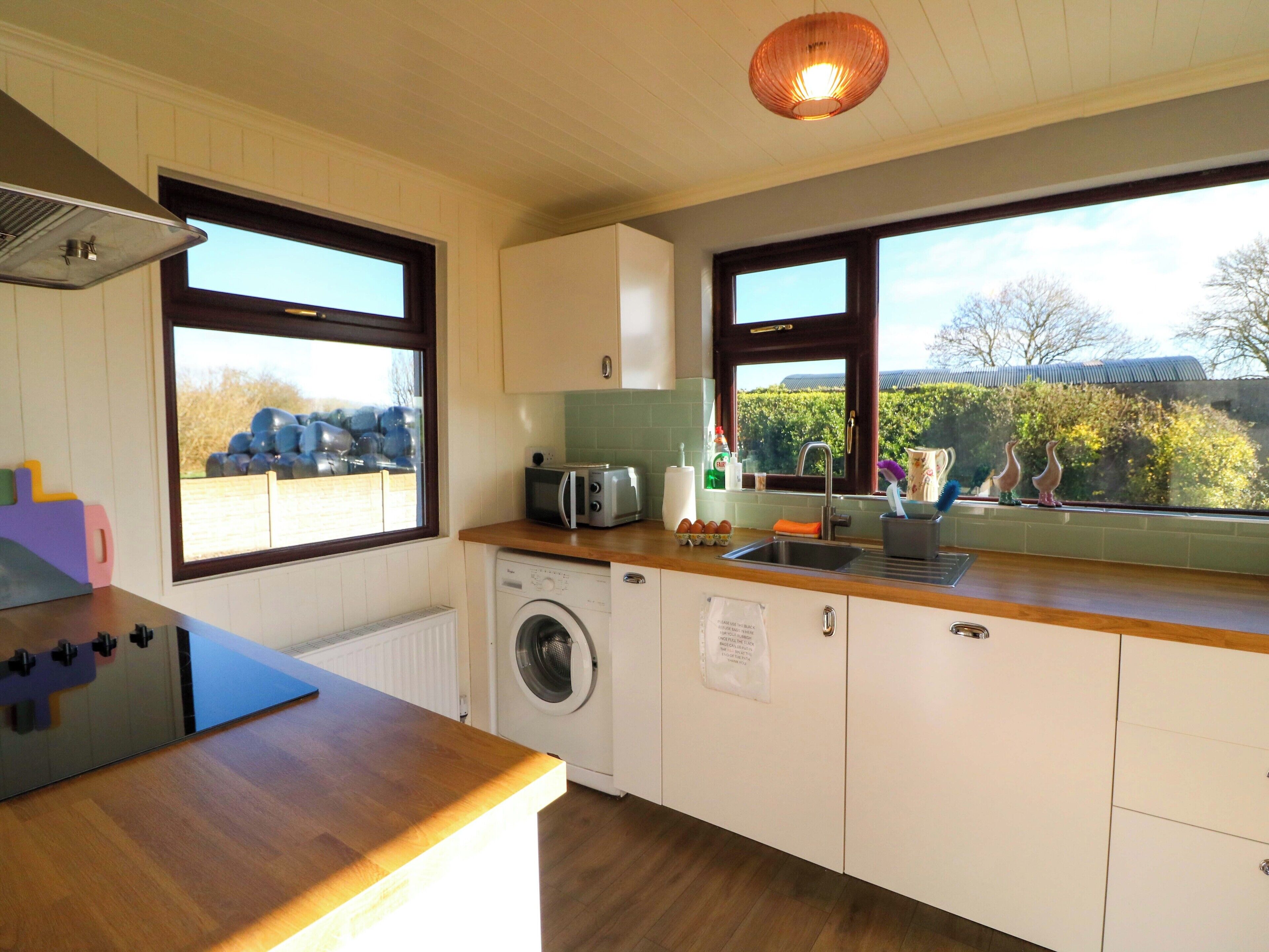 A kitchen with a washing machine, a toaster, and a window with a view of trees.