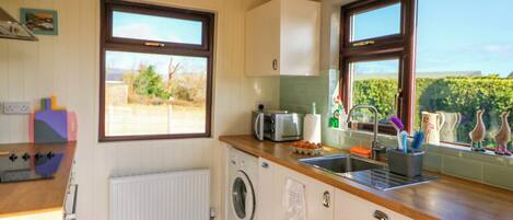 A kitchen with a washing machine, a sink, and a window with a view.