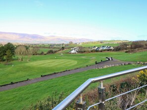 A golf course with a clear view of the green, a stone wall, and distant houses. - THADG AND HANNAH’S, pet friendly in Killorglin, County Kerry (Milltown)