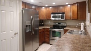Una cocina con armarios de madera, electrodomésticos de acero inoxidable, microondas integrado y un lavamanos doble.
