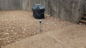 Patio con muro de concreto, una parrilla cubierta y un poste de metal.