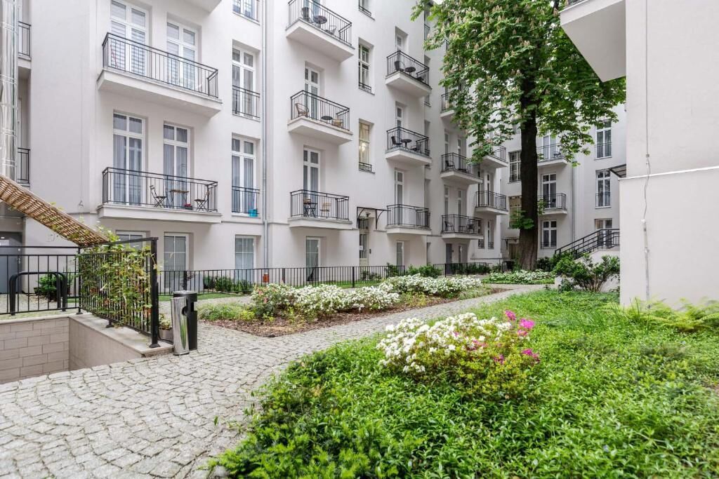 A courtyard with a cobblestone path, white buildings with balconies, and green landscaping.