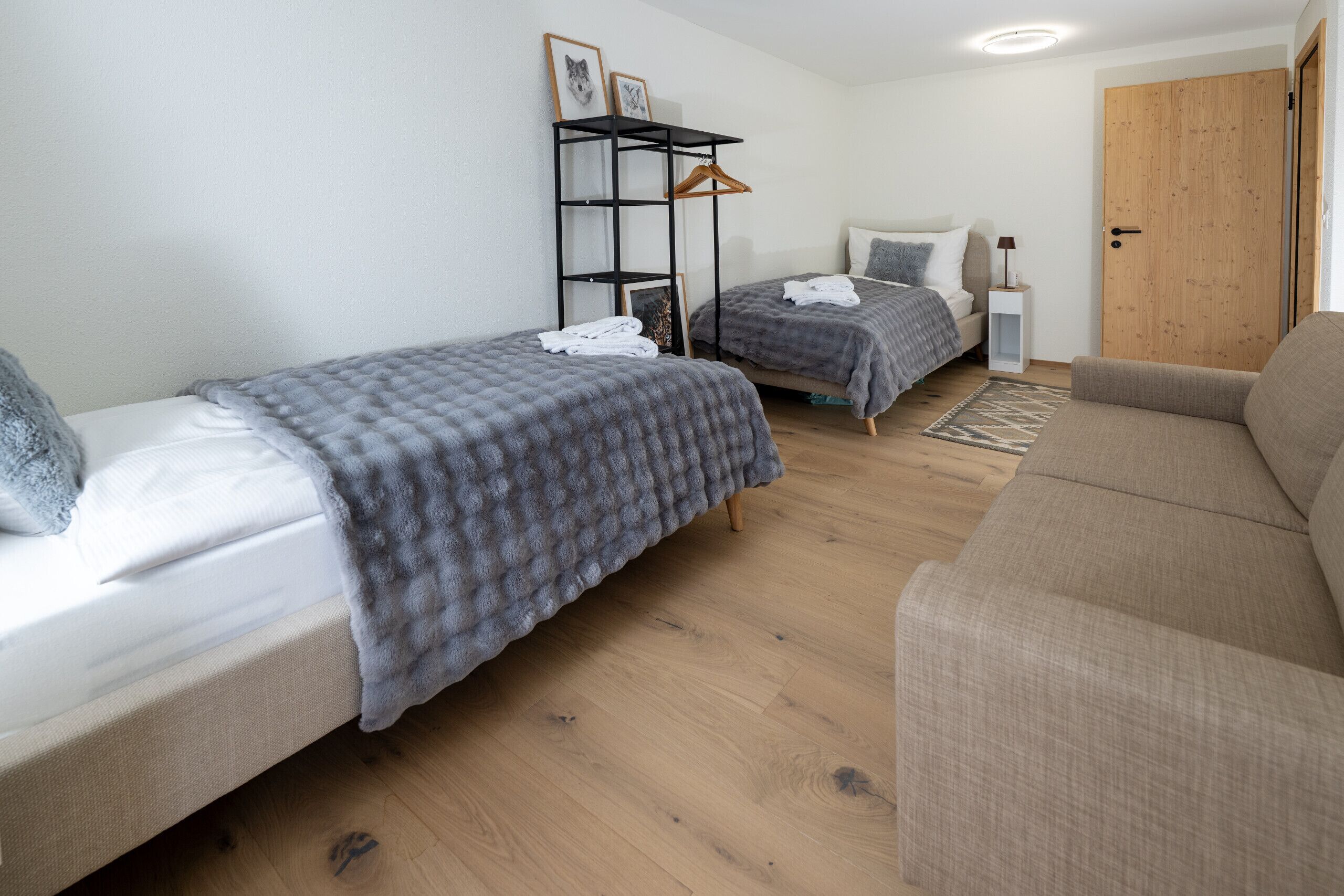 A bedroom with two beds, a sofa, a wooden floor, a wardrobe, and a door.