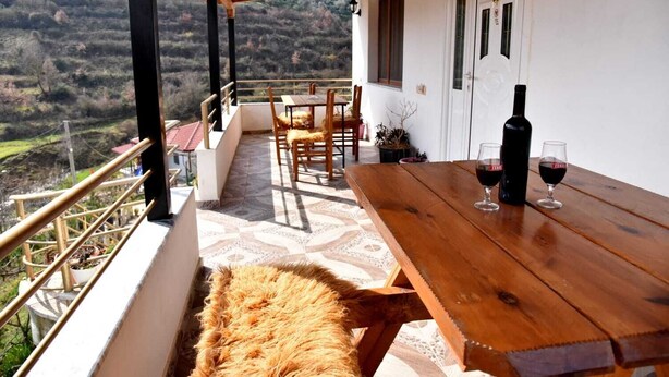 Ein Holztisch mit Weingläsern und einer Flasche auf einem Balkon mit Blick auf eine hügelige Landschaft.