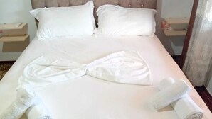 Ein ordentlich bezogenes Bett mit einem Handtuch in einer Schleife, einem aufgerollten Handtuch und einem Kissen.
