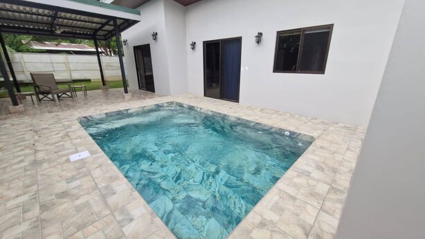 A rectangular swimming pool with a tiled deck, a covered seating area with chairs, and a white building with windows and doors. - House With a Private Pool (Ciudad Cortés)