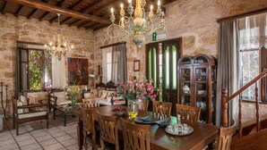A rustic dining area with a wooden table, chairs, a chandelier, and a stone wall. - Kissamos Villa in Crete Island (Kissamos)