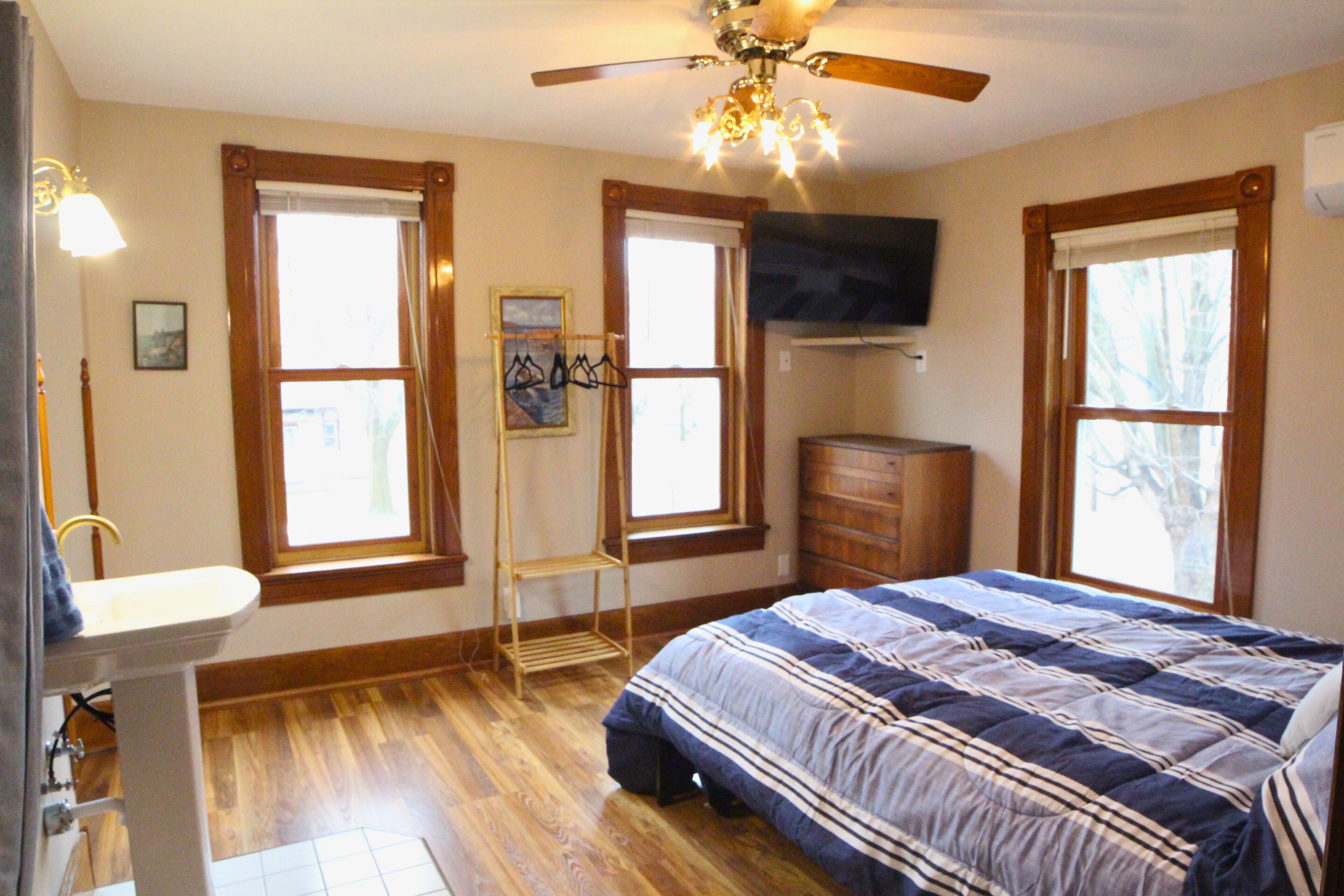 A bedroom with a bed, dresser, vanity, and a ceiling fan.
