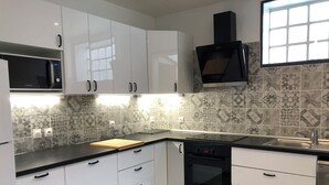 A modern kitchen with white cabinets, a Bosch dishwasher, a microwave, and a black range hood. - Luxury apartment line 14 IGR Paul Brousse Paris (Villejuif)
