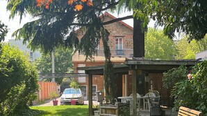 A backyard with a wooden bench, a covered patio area, and a stone house in the background. - Luxury apartment line 14 IGR Paul Brousse Paris (Villejuif)