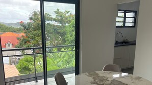 Ein Essbereich mit rundem Tisch und Stühlen, eine Schiebeglastür, die auf einen Balkon führt, und eine durch eine angrenzende Tür erkennbare Küche.