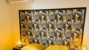 Ein Bett mit einem gemusterten Kopfteil, zwei Nachttischlampen und einer Klimaanlage an der Wand.
