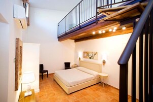 Un dormitorio con una cama, una silla, una mesita de noche, una lámpara, un cuadro y una escalera.