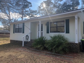 A single-story house with a front porch, a visible number '101' on the right side, and a small garden with palm plants. - Cute 2-bedroom cottage in Oak Island only minutes from the beach (Oak Island)