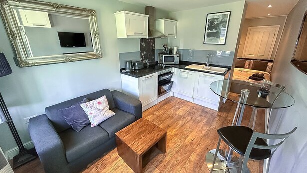 Un espacio habitable compacto con sofá, mesa de centro, kitchenette y una mesa de comedor de vidrio.
