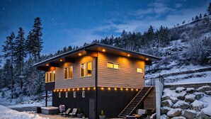 Een moderne chalet met een overdekte buiten zithoek, een trap en uitzicht op het besneeuwde landschap.