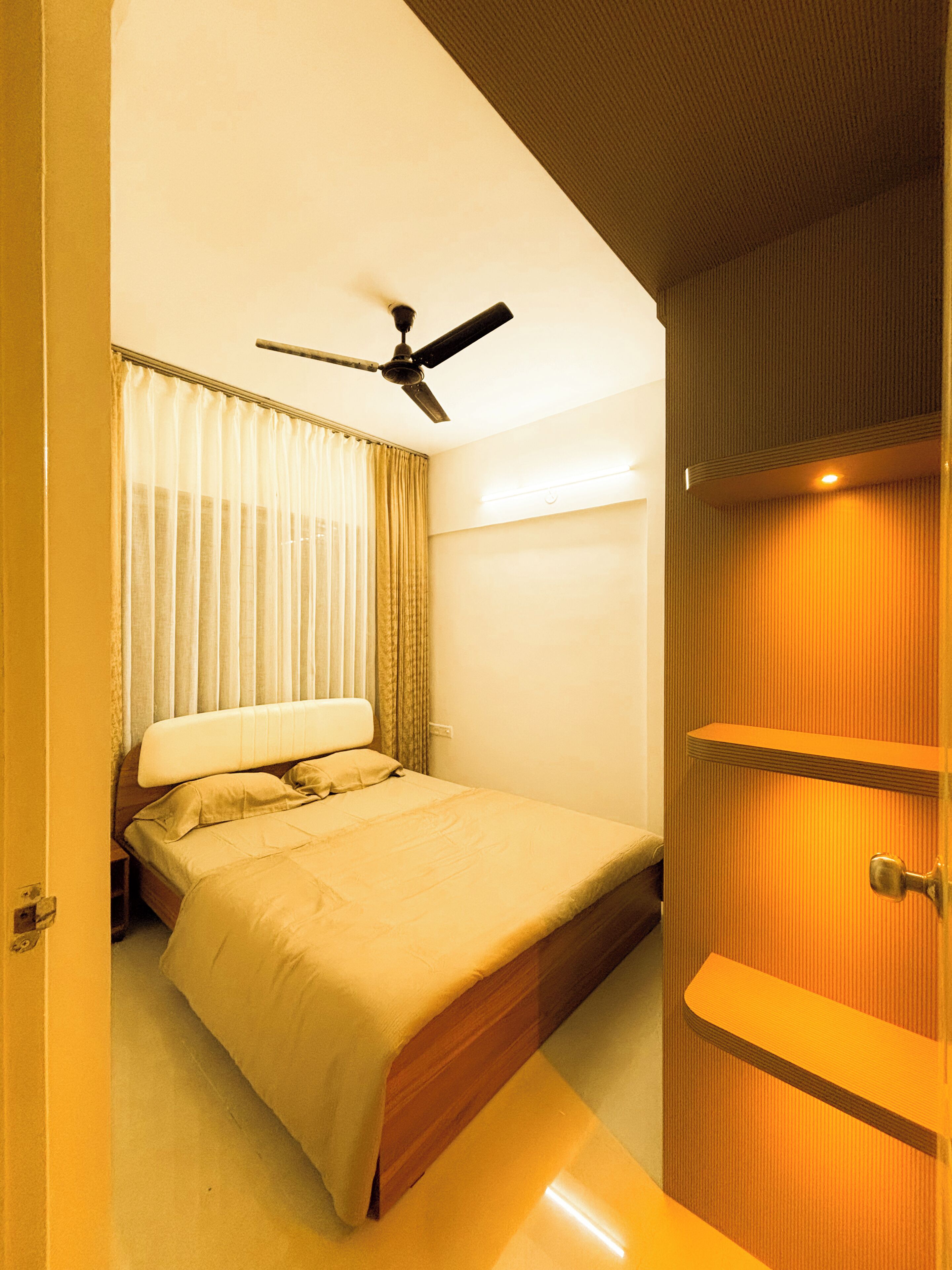 Une chambre à coucher avec un lit, des rideaux, un ventilateur de plafond et une armoire en bois.