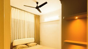 Une chambre à coucher avec un lit, des rideaux, un ventilateur de plafond et une armoire en bois.