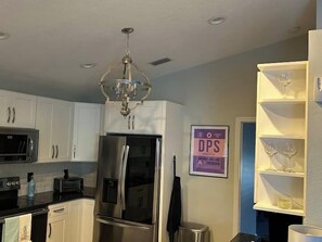 A modern kitchen with stainless steel appliances, a chandelier, and a sign indicating a dry cleaning service. - Private Pool Retreat Near New Smyrna Beach (New Smyrna Beach)