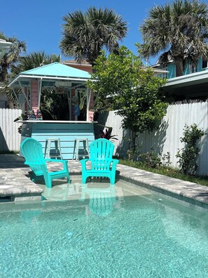 A swimming pool with two turquoise Adirondack chairs, a covered seating area, and a white fence with greenery. - Private Pool Retreat Near New Smyrna Beach (New Smyrna Beach)
