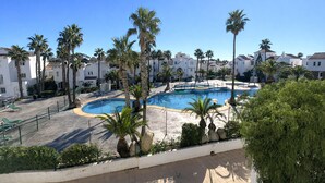 A pool area with palm trees, a clear blue sky, and white buildings in the background. - Apartment With Pool and Golf Course Views in Roquetas de Mar (Roquetas de Mar)