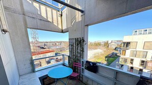Ein Balkon mit Tisch und Stühlen, Blick auf die Stadtlandschaft, und ein Gebäude mit markanter Architektur.