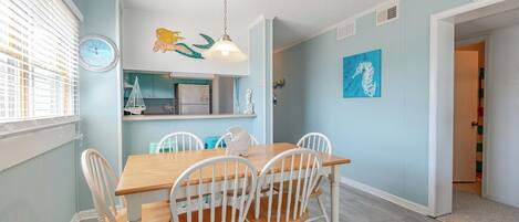 A dining area with a wooden table and white chairs, a wall clock, and a seahorse painting.