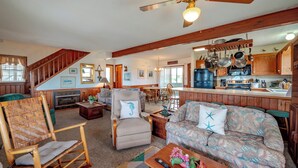 A spacious living room with a fireplace, a dining area, and a kitchen with wooden cabinets and a large island. - JL #296 | East Of Eden - Semi-Oceanfront - Horizon Ocean View - Private Pool (Nags Head)