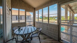 A covered porch with a table and chairs, large windows, and a view of the surrounding area. - JL #296 | East Of Eden - Semi-Oceanfront - Horizon Ocean View - Private Pool (Nags Head)