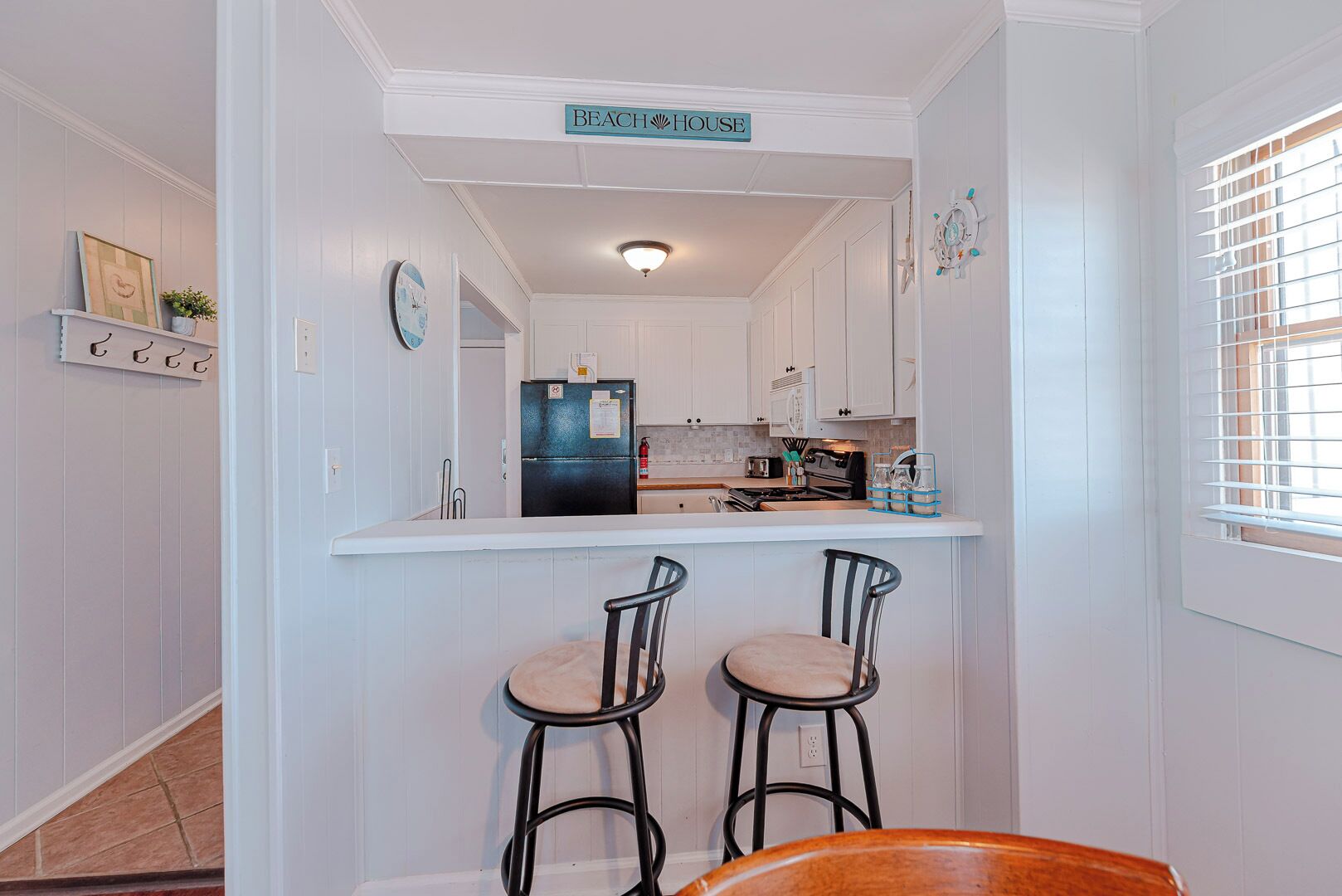 A kitchen with white cabinets, a black refrigerator, a bar counter, and two bar stools.