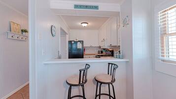 A kitchen with white cabinets, a black refrigerator, a bar counter, and two bar stools.