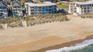 Un hôtel situé en bord de mer, composé de plusieurs bâtiments à étages, avec une plage de sable et des vagues déferlantes.