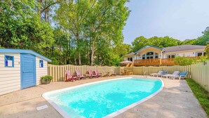 Um quintal com piscina, espreguiçadeiras, deck de madeira e uma casa com cerca.