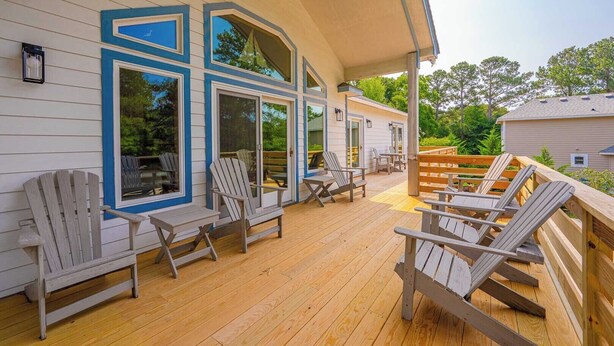 Um deck coberto com cadeiras Adirondack e um corrimão de madeira, com vista para um jardim.