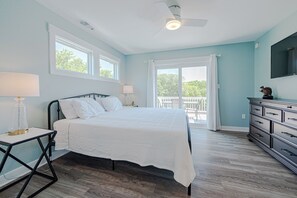 A bedroom with a bed, a dresser, a nightstand, a lamp, a ceiling fan, and a balcony with outdoor furniture. - JL #034 - Solitude House - Oceanside - Private Pool - Hot Tub (Southern Shores)