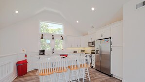 A kitchen with white cabinets, a stainless steel refrigerator, a microwave, and a red trash bin. - JL #034 - Solitude House - Oceanside - Private Pool - Hot Tub (Southern Shores)