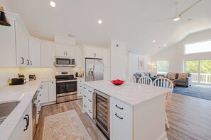 A modern kitchen with white cabinetry, a central island, and a dining area with a blue rug. - JL #034 - Solitude House - Oceanside - Private Pool - Hot Tub (Southern Shores)