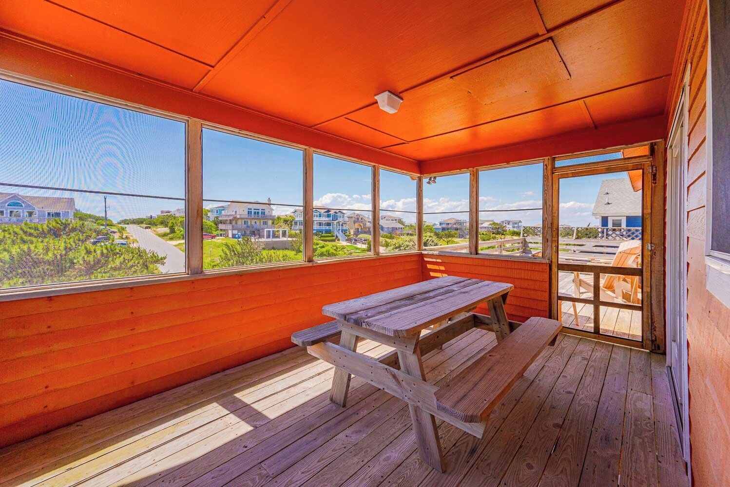 A wooden deck with a picnic table, large windows, and a view of houses.