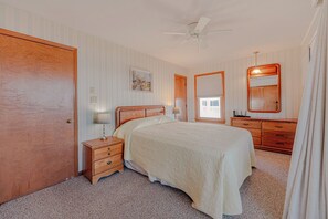 A bedroom with a bed, nightstand, dresser, mirror, and a ceiling fan. - JL #228 | Tengerhaz | Oceanfront | Ocean Views (Duck)