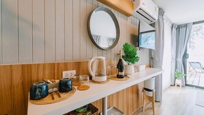 A modern kitchen with wooden paneling, a white countertop, a round mirror, a coffee maker, and a plant. - Sea Sand See Sky Beach Front Resort (Thep Krasattri)