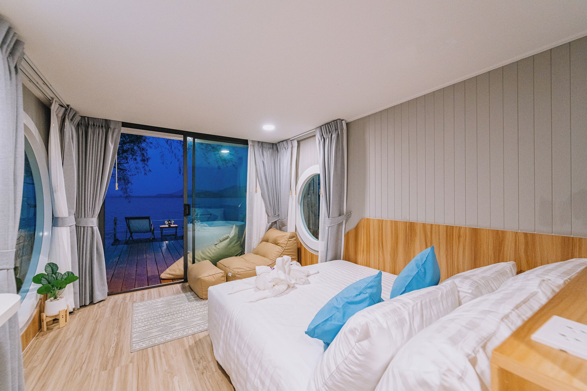 A hotel room with a bed, a small table, a chair, and a view of the sea.