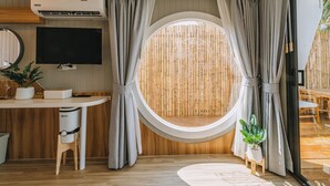A room with a round window, a TV, a desk, a chair, and a small plant. - Sea Sand See Sky Beach Front Resort (Thep Krasattri)