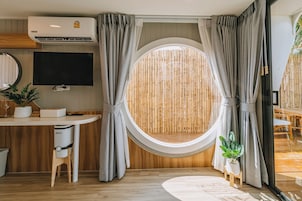 Una habitación con ventanal redondo, televisor, escritorio, silla y una pequeña planta.