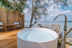 Una terraza de madera con un jacuzzi, mobiliario de madera y vistas al mar.