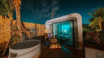 A modern outdoor bathroom with a glass enclosure, a hot tub, and a wooden deck.