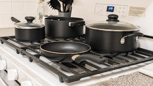 Una cucina con fornello a gas, pentole, padelle e una sveglia digitale.