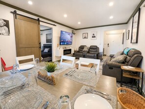 Ein modernes Wohnzimmer mit Essbereich, einem an der Wand montierten Fernseher und einer Schiebetür zu einem weiteren Raum.