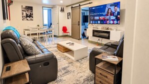 Un soggiorno moderno con un divano in pelle nera, un tavolino da caffè bianco e una TV a schermo piatto montata a parete.
